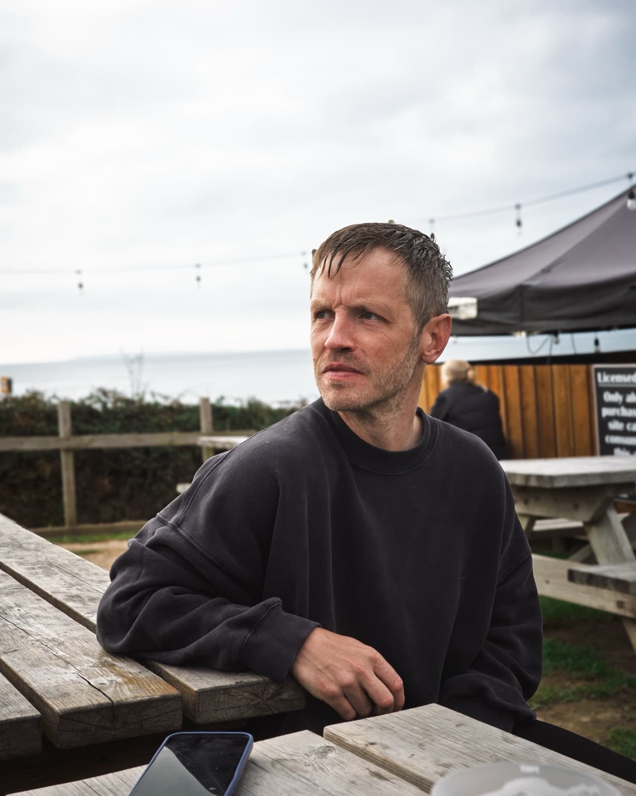 Phil Smith at a picnic table on the seafront, looking out to sea